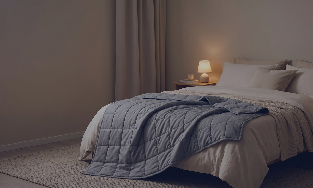 Couverture lestée Lestona, coloris bleu marine, dépliée sur un lit dans une chambre le soir, lampe de chevet allumée.